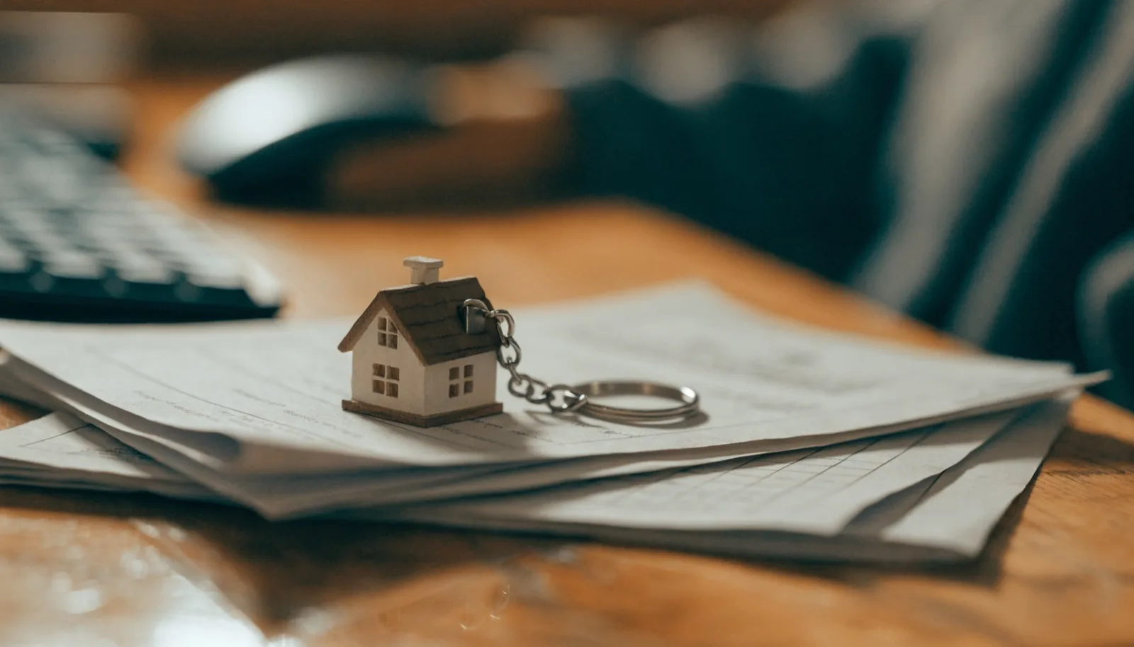 Portachiavi a forma di casa appoggiato su documenti assicurativi su una scrivania in legno