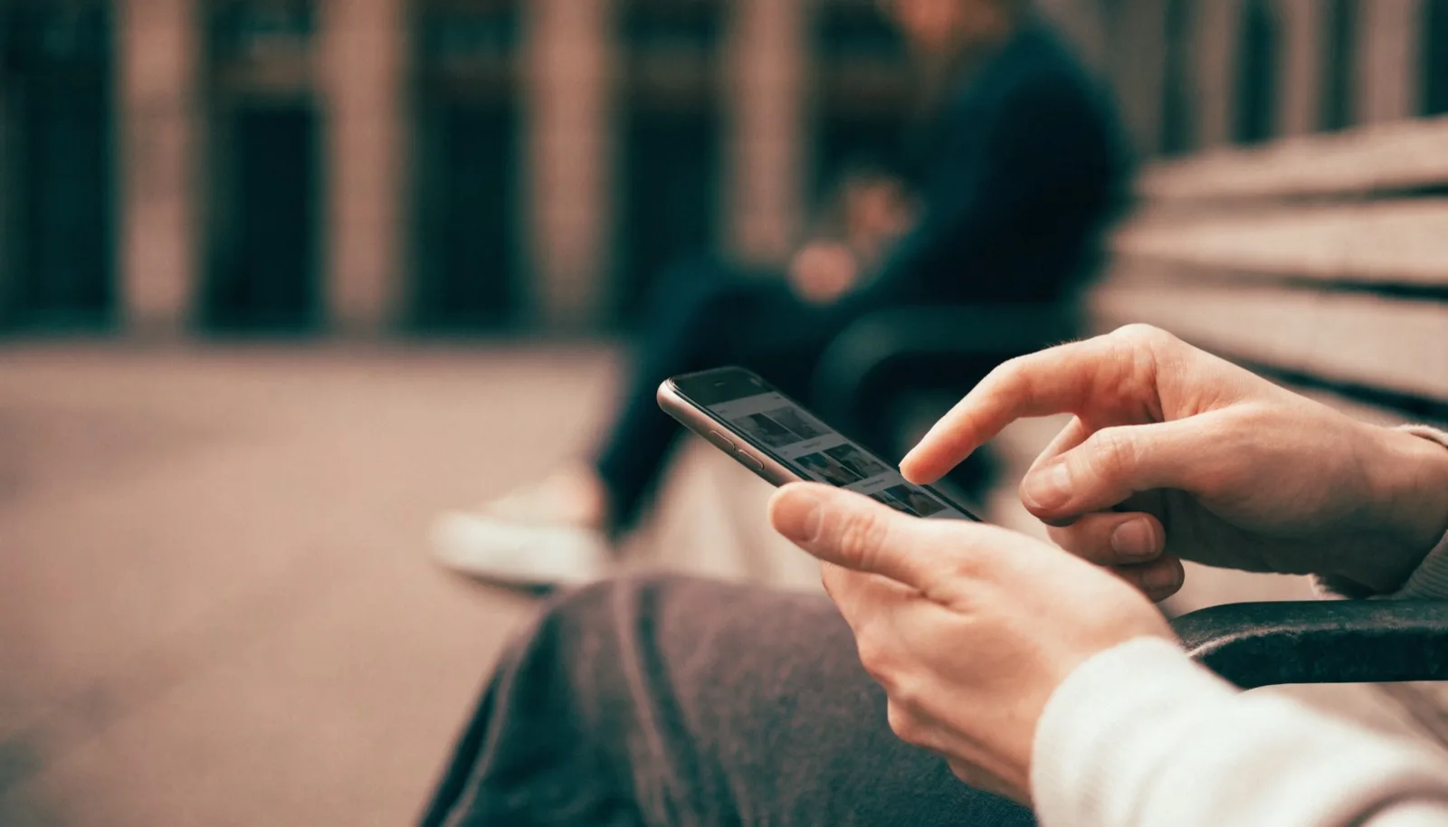 Mani che tengono uno smartphone mentre si sfoglia un'app di annunci, seduti su una panchina all'aperto